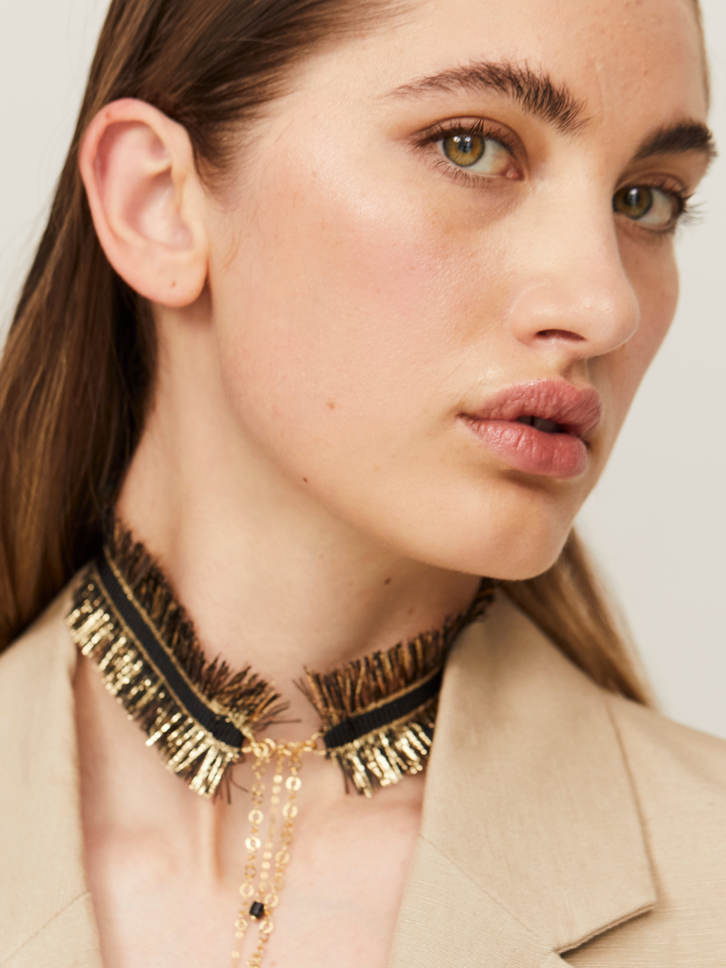 Exzentrische Halskette in Schwarz und Gold, getragen von einer jungen, attraktiven Frau, die zusätzlich einen hellen Blazer trägt und in die Kamera guckt.