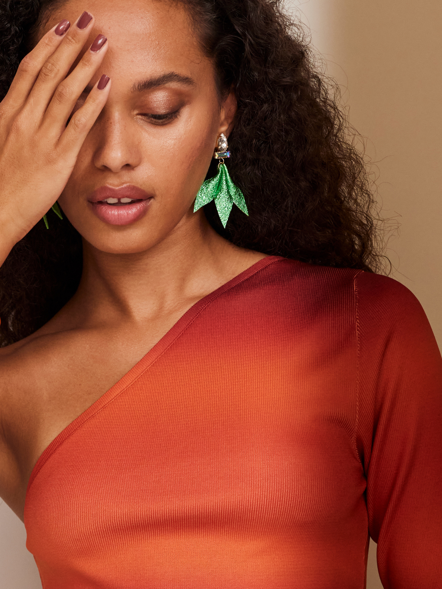 Attraktive Frau im roten Kleid trägt ein wunderschönes buntes Armband sowie wunderschöne grüne Ohrringe, die ihr lockiges, braunes Haar unterstreichen.