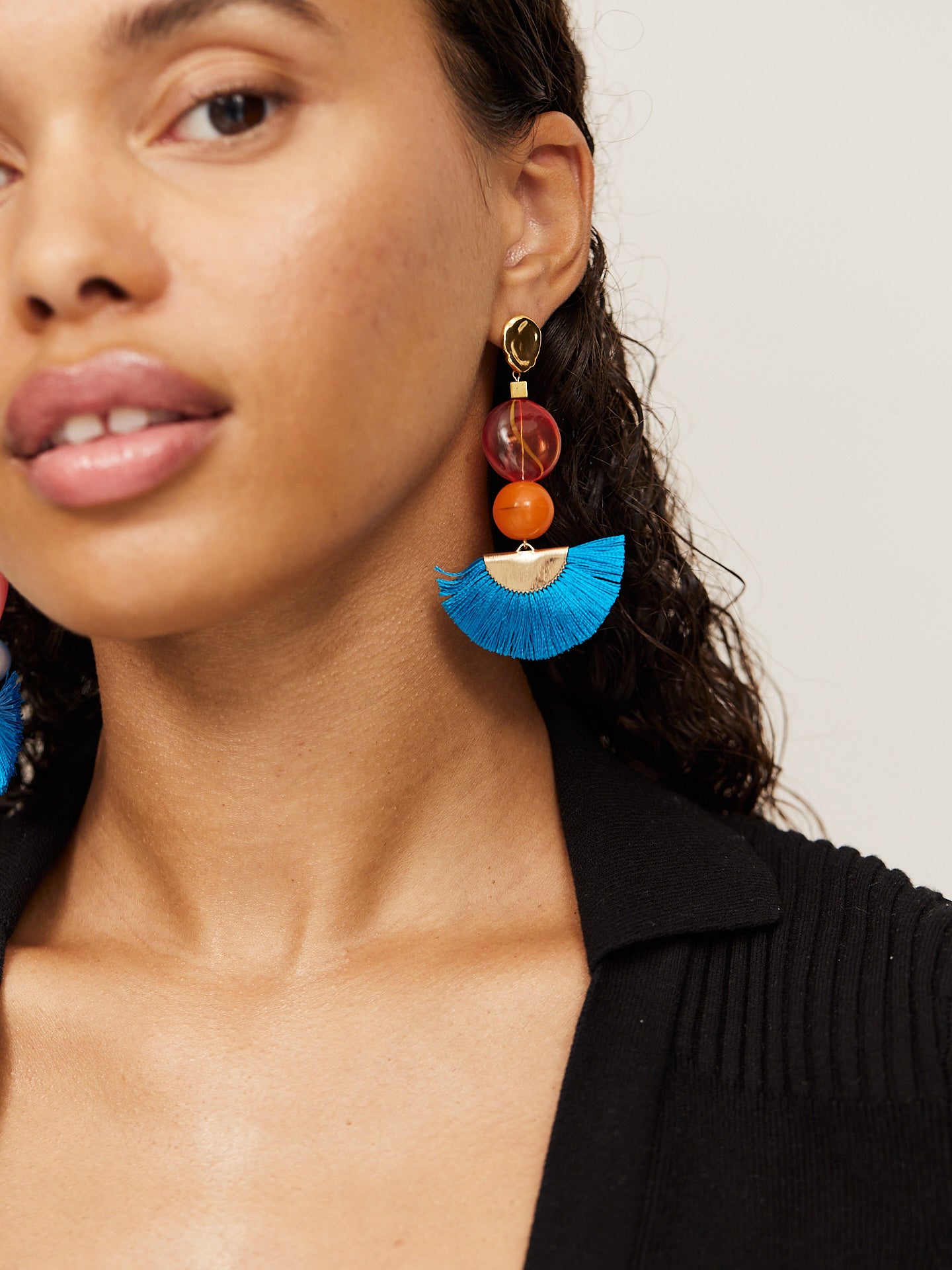 Attraktive Frau mit braunen Augen trägt einen schwarzen Body und aufregende Ohrringe mit einem tollen blauen Fächer und einer orangefarbenen Perle