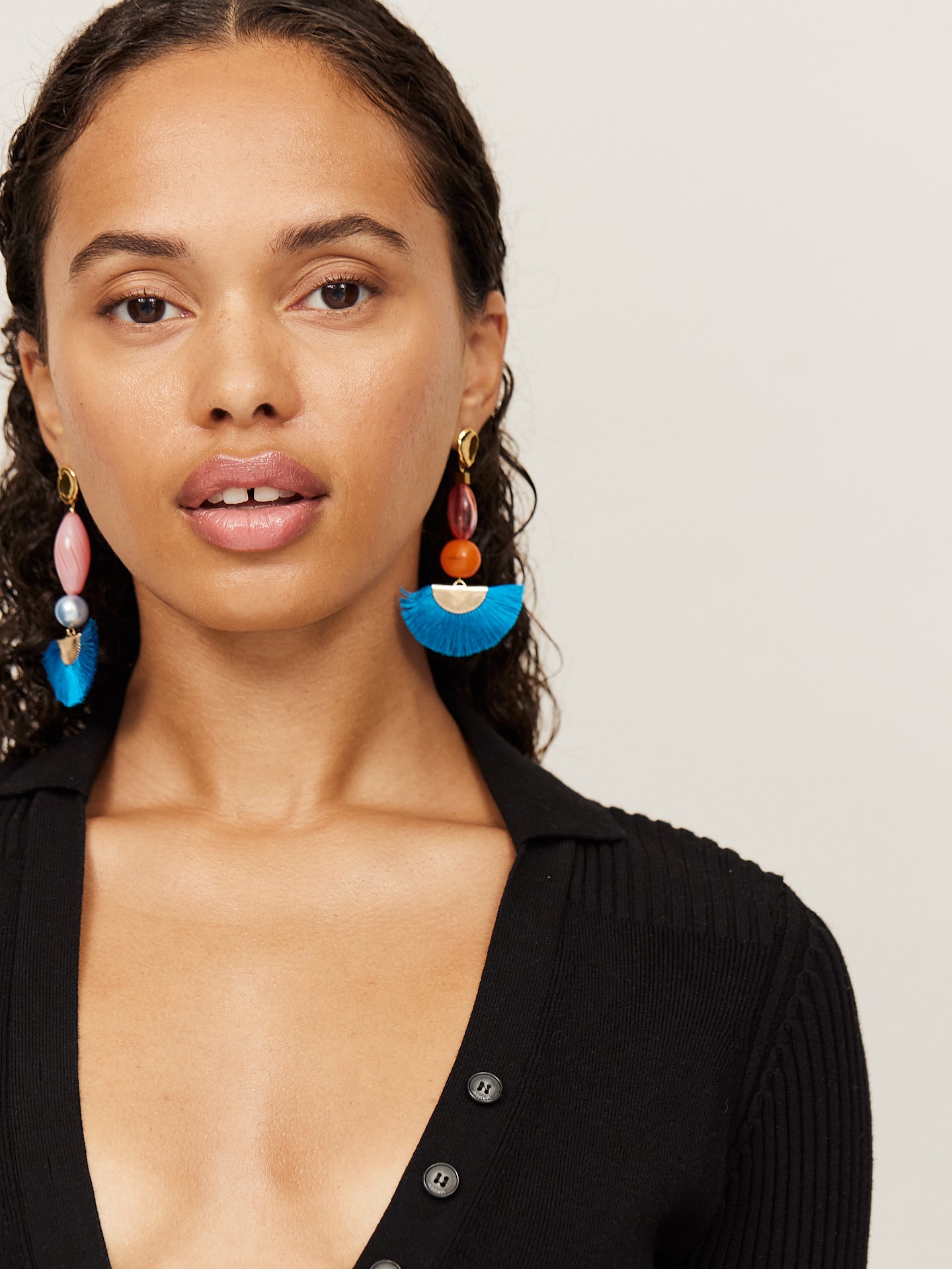 Attraktive Frau mit braunen Augen trägt einen schwarzen Body und aufregende Ohrringe mit einem tollen blauen Fächer und einer orangefarbenen Perle. Der asymmetrische andere Ohrringe ist farblich ähnlich, in seiner Form aber etwas länger.