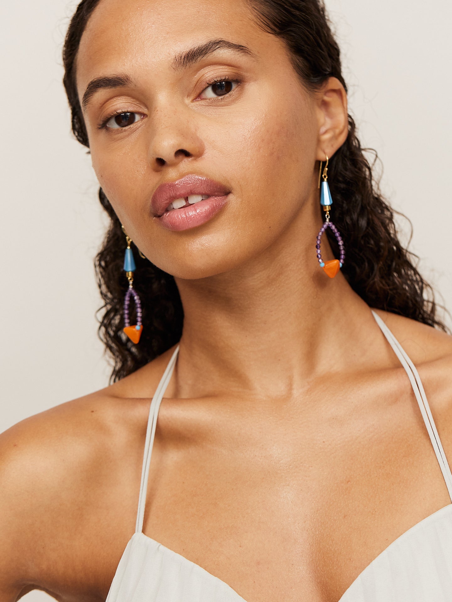 Aufregende, attraktive Frau mit dunklem Teint und dunklen Augen schaut in die Kamera und trägt dabei kreative, bunte Ohrringe mit einer orangenen Perle.