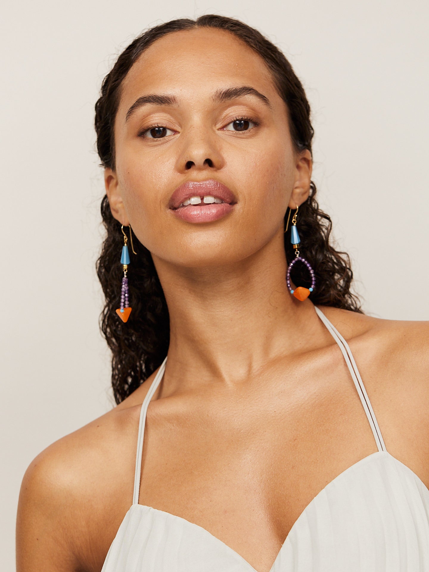 Aufregende, attraktive Frau mit dunklem Teint und dunklen Augen schaut in die Kamera und trägt dabei kreative, bunte Ohrringe mit einer orangenen Perle.