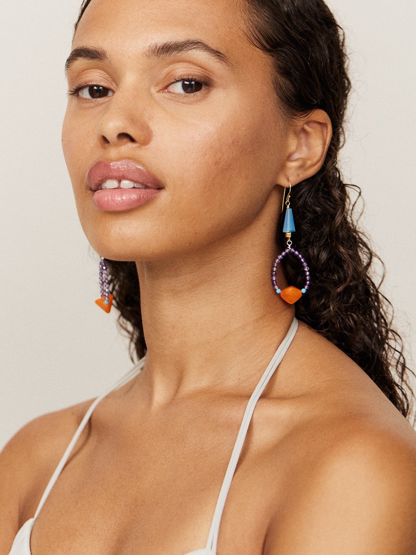 Aufregende, attraktive Frau mit dunklem Teint und dunklen Augen schaut in die Kamera und trägt dabei kreative, bunte Ohrringe mit einer orangenen Perle.