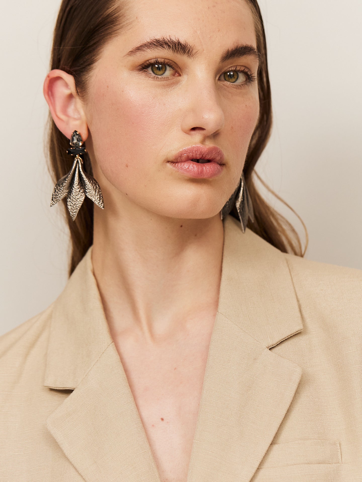 Attraktive Frau mit braunen Augen und sinnlichen Lippen, trägt einen hellen Blazer und helle Nappa Leder Ohrringe mit dunklem Stecker.