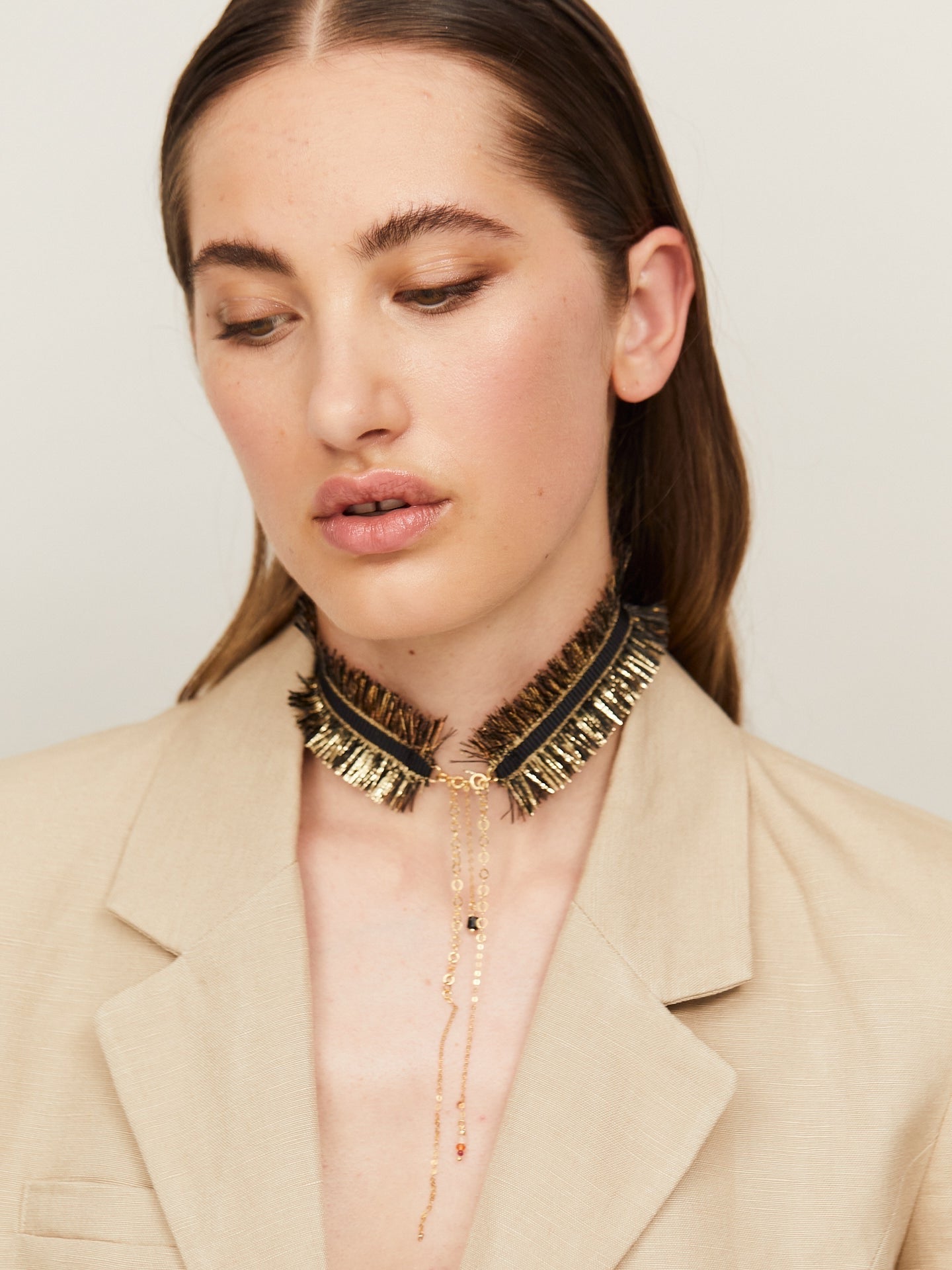 Exzentrische Halskette in Schwarz und Gold, getragen von einer jungen, attraktiven Frau, die zusätzlich einen hellen Blazer trägt.