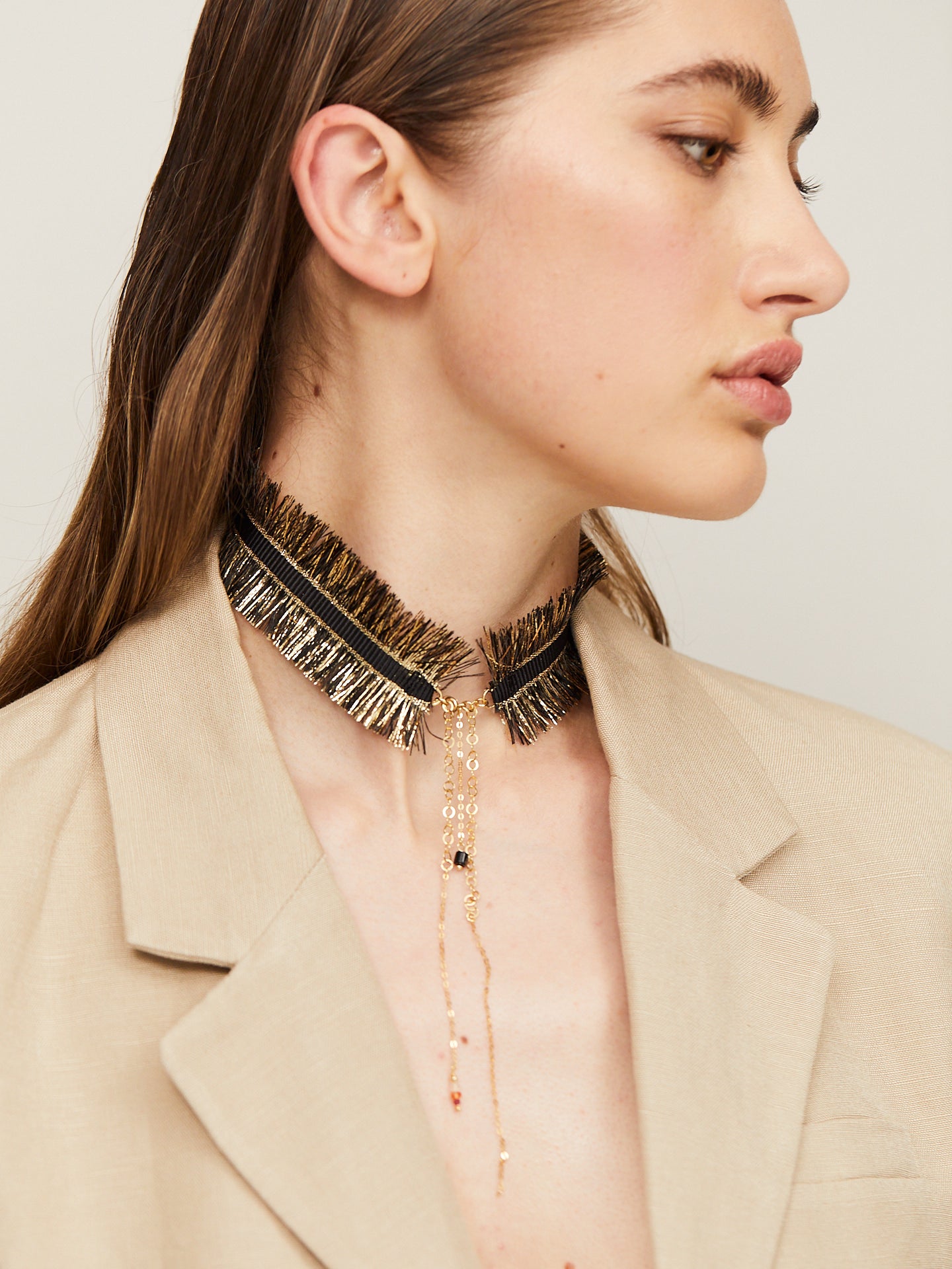 Exzentrische Halskette in Schwarz und Gold, getragen von einer jungen, attraktiven Frau, die im Profil zu Boden guckt.