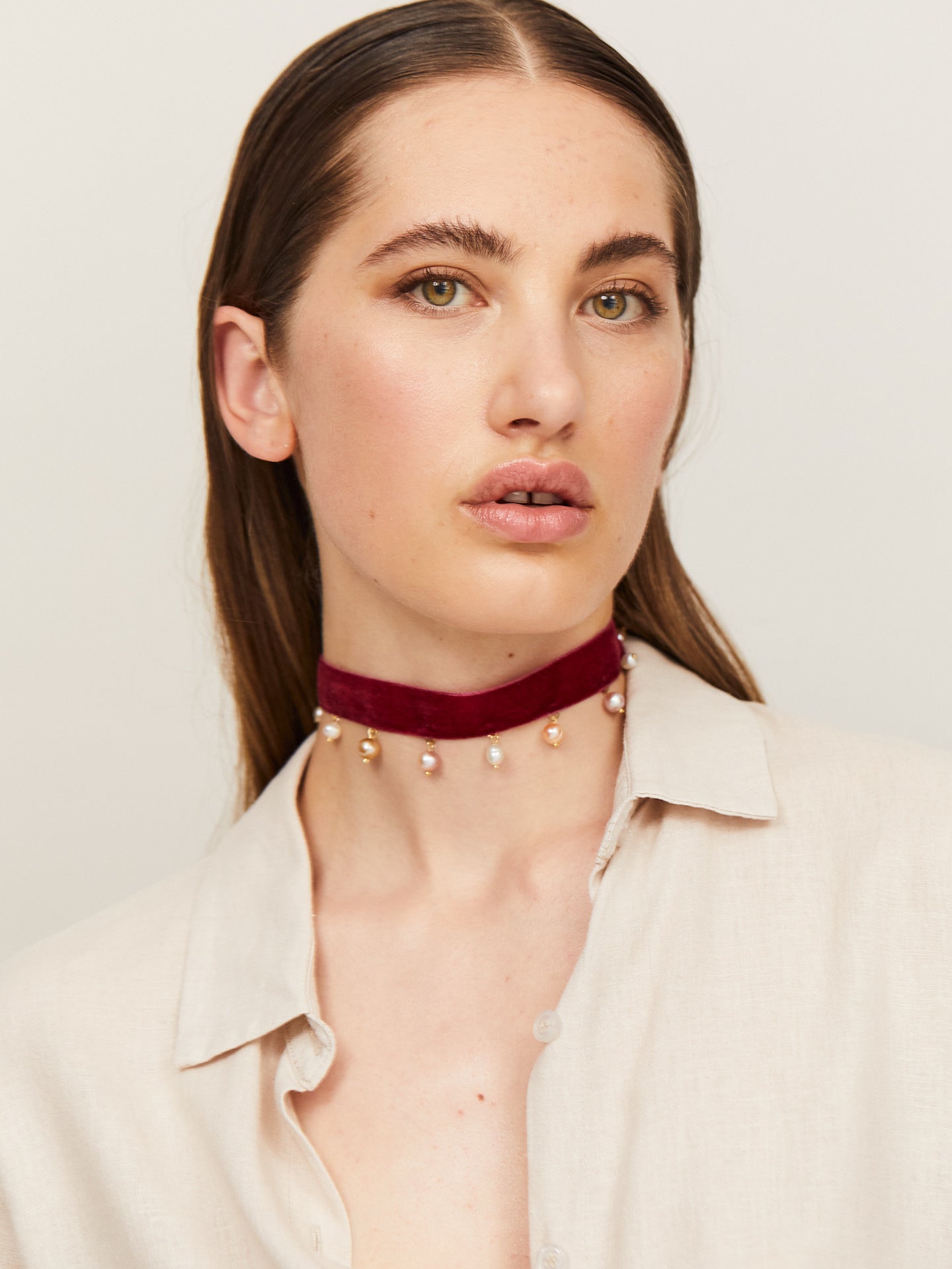 Eine Frau mit sinnlichen Lippen und braunen Augen schaut in die Kamera und trägt dabei einen handgefertigten Choker, an dem Perlen in Abständen hängen.