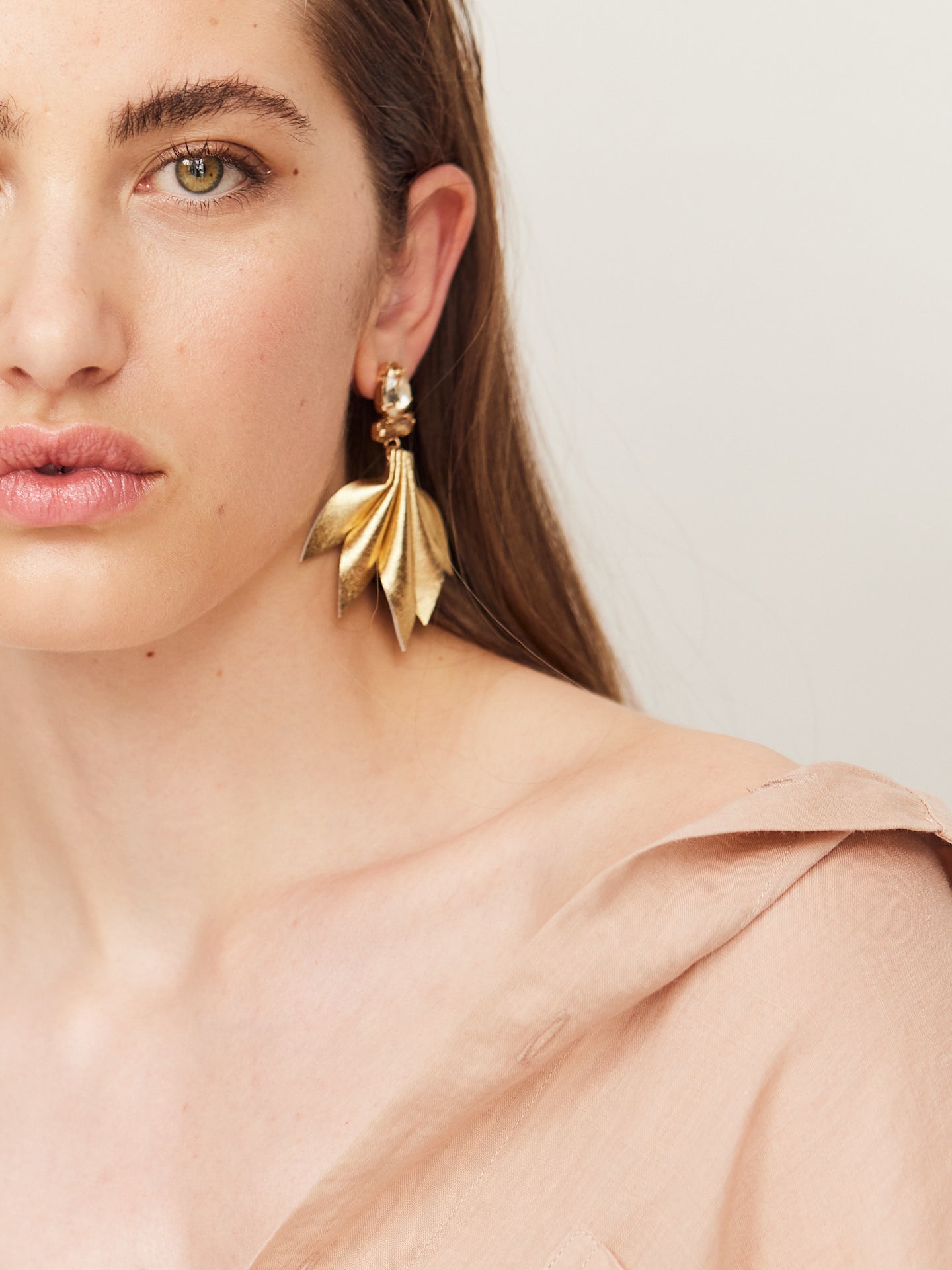 Attraktive Frau mit braunen Augen und braunen Haaren und trägt goldene Nappa Leder Ohrringe und schaut direkt in die Kamera.