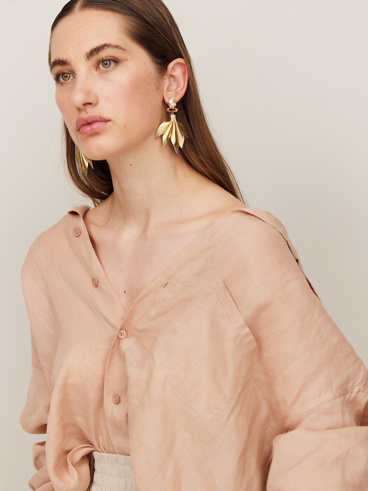 Attraktive Frau mit braunen Augen und braunen Haaren und trägt goldene Nappa Leder Ohrringe und schaut verträumt an der Kamera vorbei.