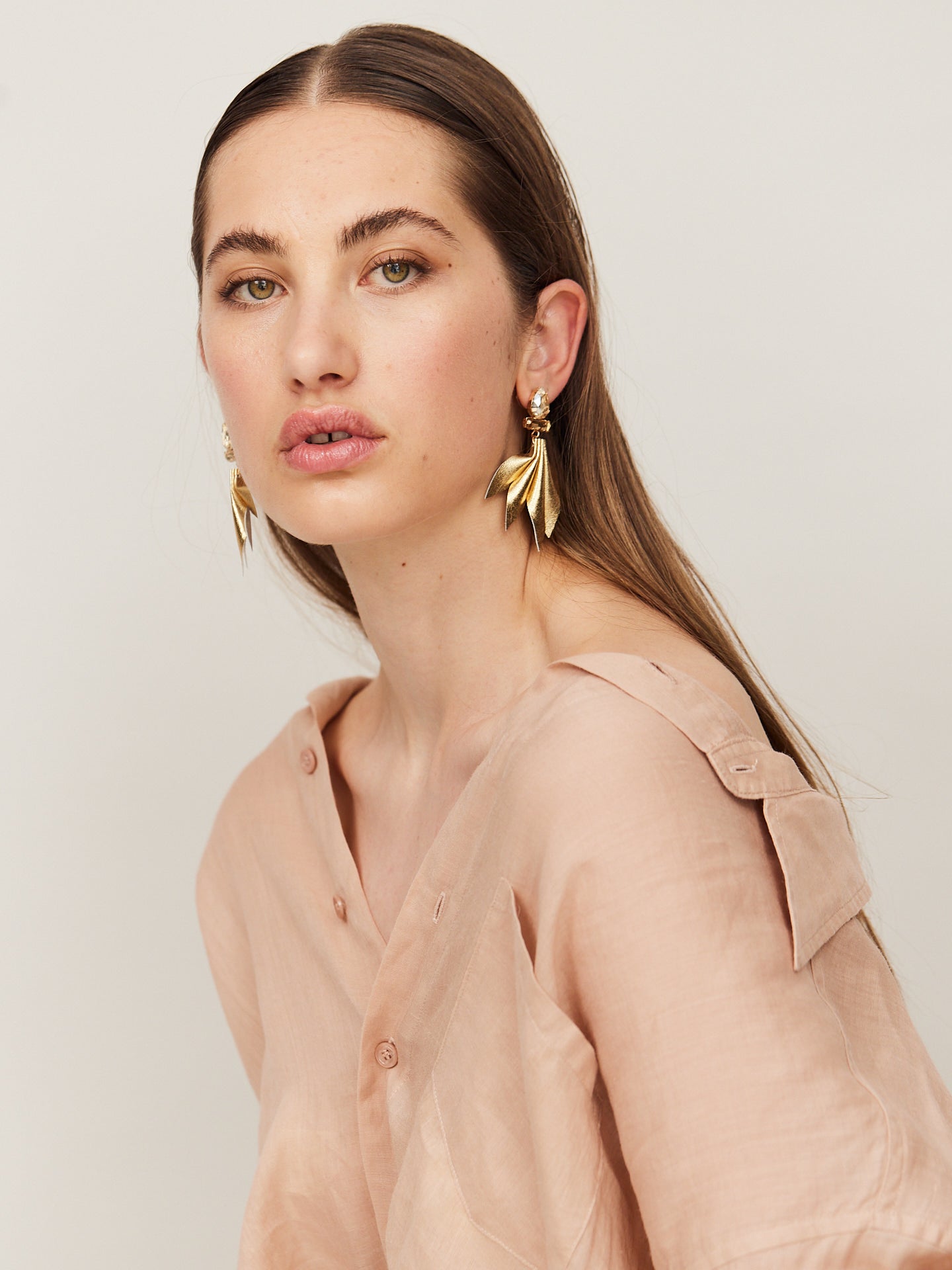 Attraktive Frau mit braunen Augen und braunen Haaren und trägt goldene Nappa Leder Ohrringe und schaut direkt in die Kamera.