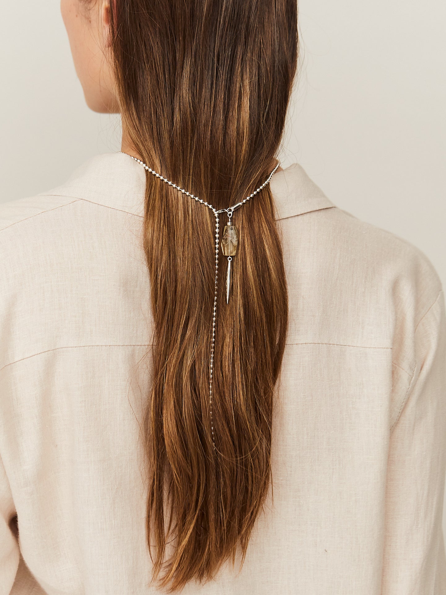 Braunhaarige Frau trägt eine zarte silberne Kette mit einem aufregenden Anhänger im Haar.