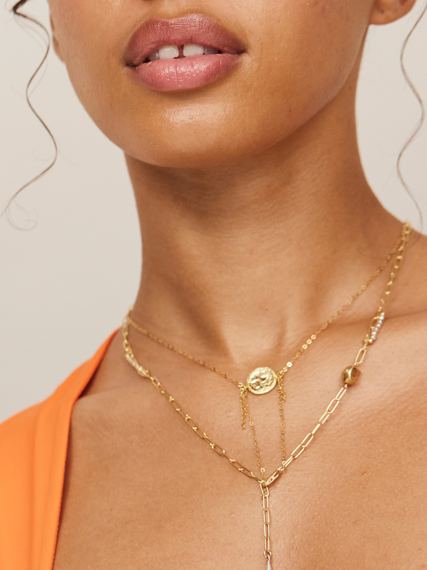 Attraktive Frau mit vollen Lippen trägt 2 Halsketten in Gold.