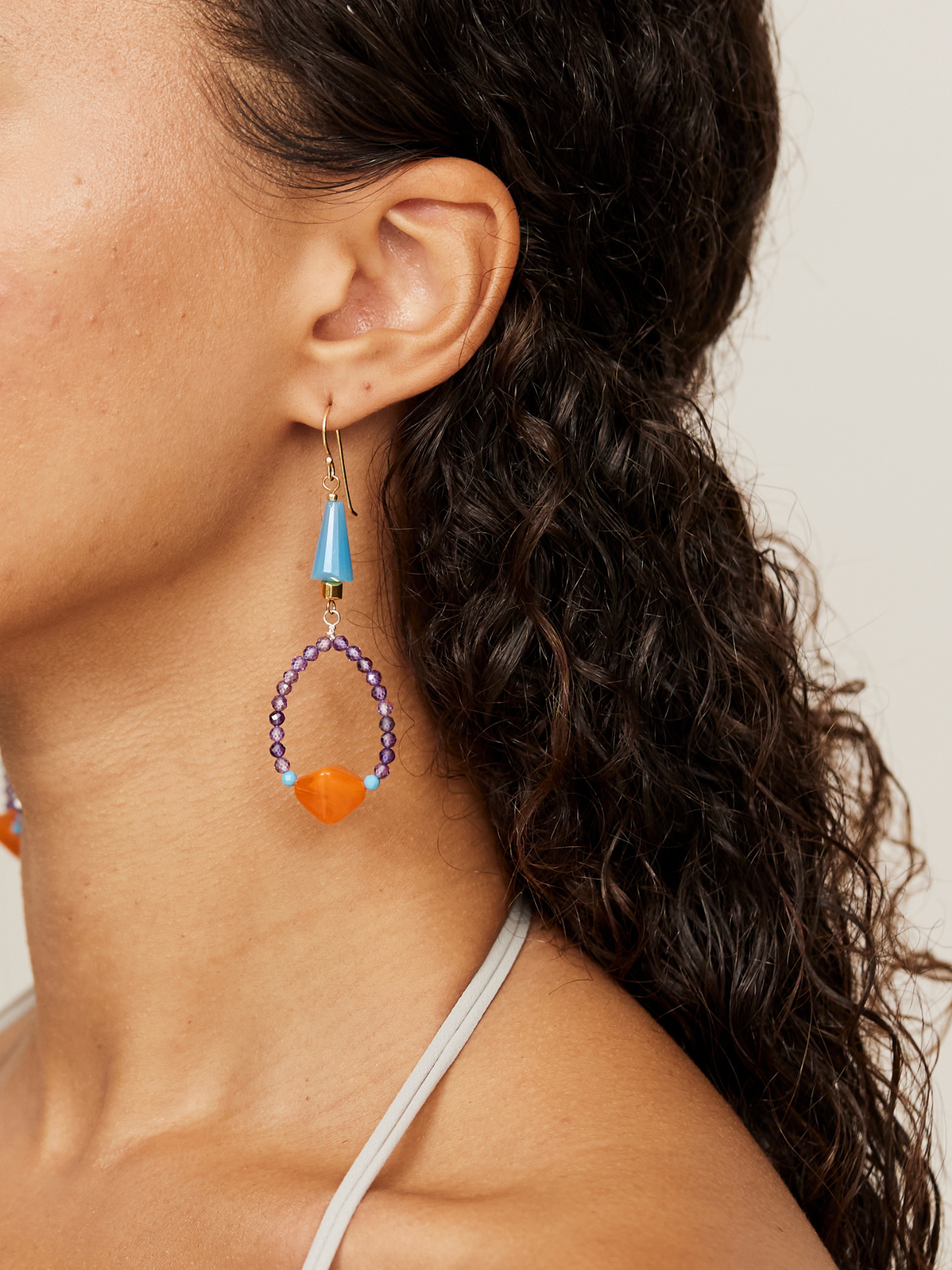 Großaufnahme eines wunderschönen, bunten Ohrrings, der aus violetten, blauen Steinen und einer Orangenen Perle besteht.