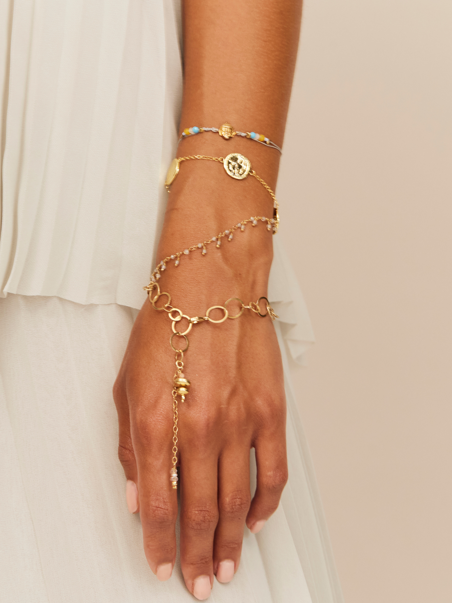 Frau trägt eine Kombi an Armbändern mit goldenen Gliedern, einer Münze als Anhänger und einigen aufregenden Perlen und goldenem Buddha Anhänger