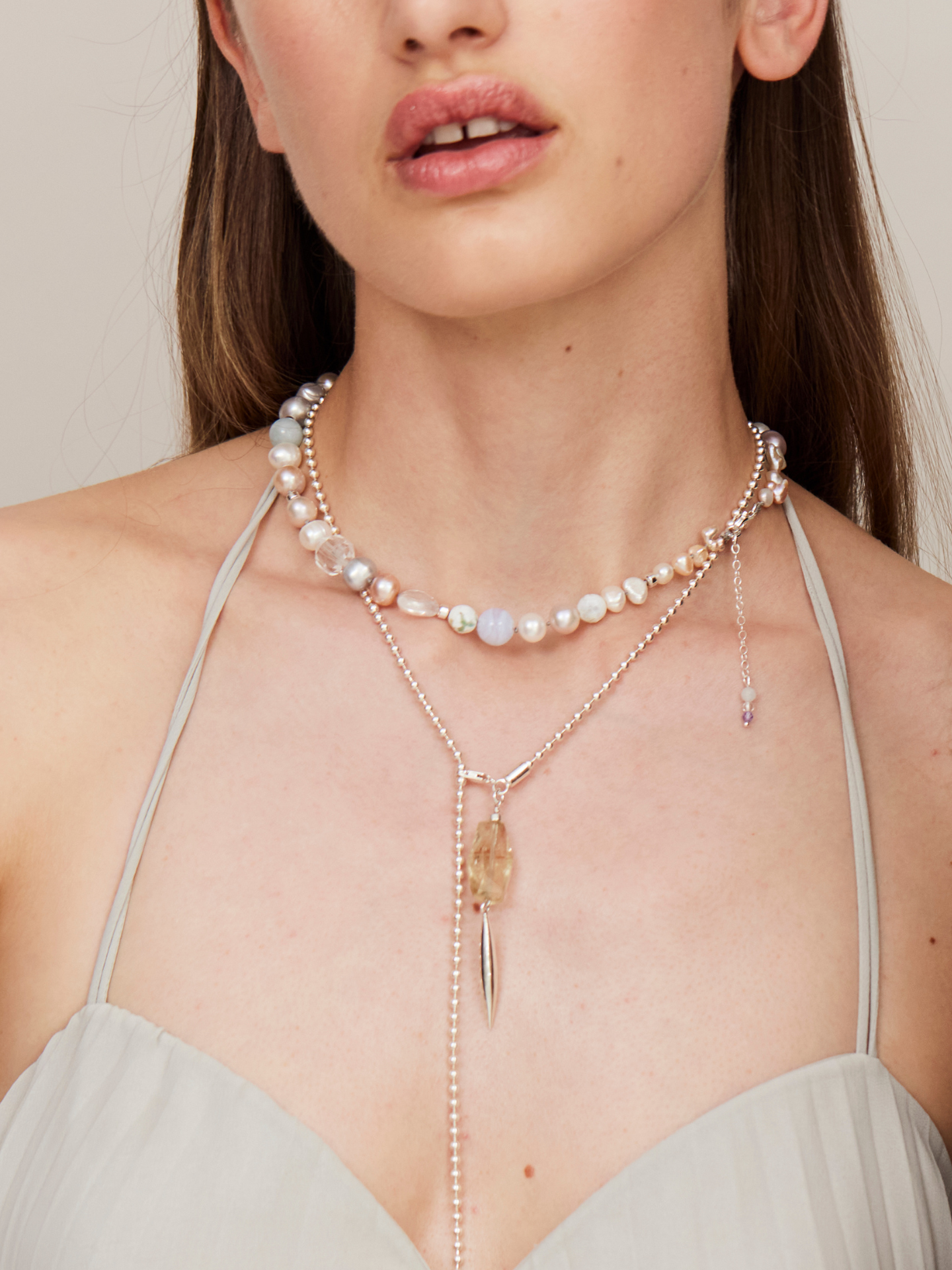 Frau mit vollen Lippen trägt eine edle Halskette mit Perlen und Anhängern in verschiedenen Längen.