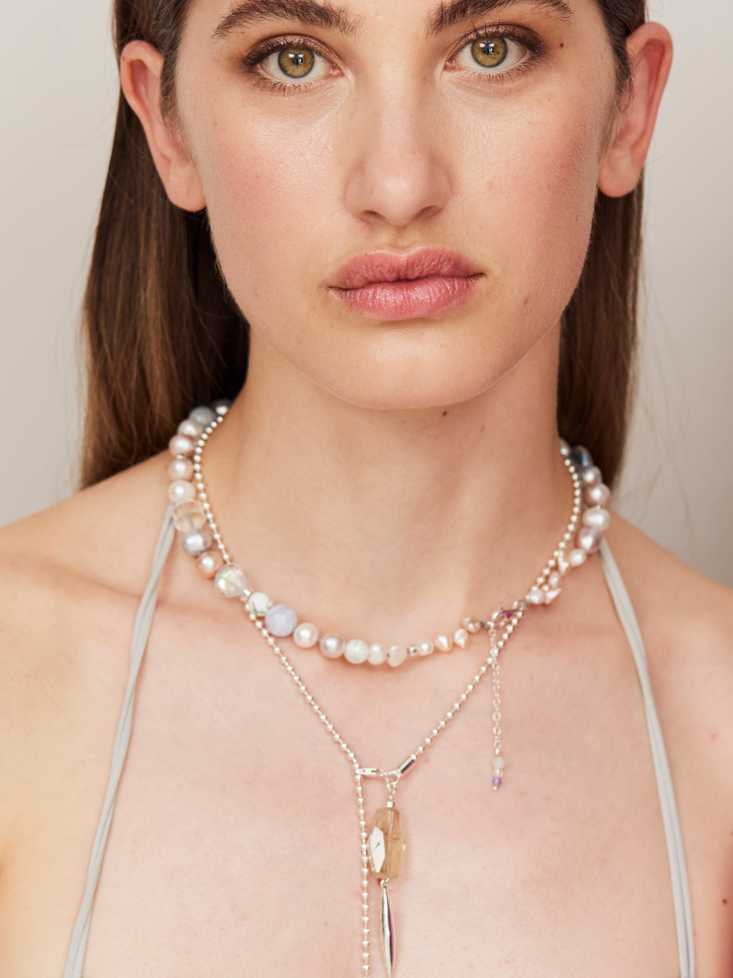 Eine Frau mit braunen Augen blickt in die Kamera und trägt eine wunderschöne, besondere Halskette, bestehend aus Perlen und verschiedenen Ketten uín unterschiedlichen Längen.