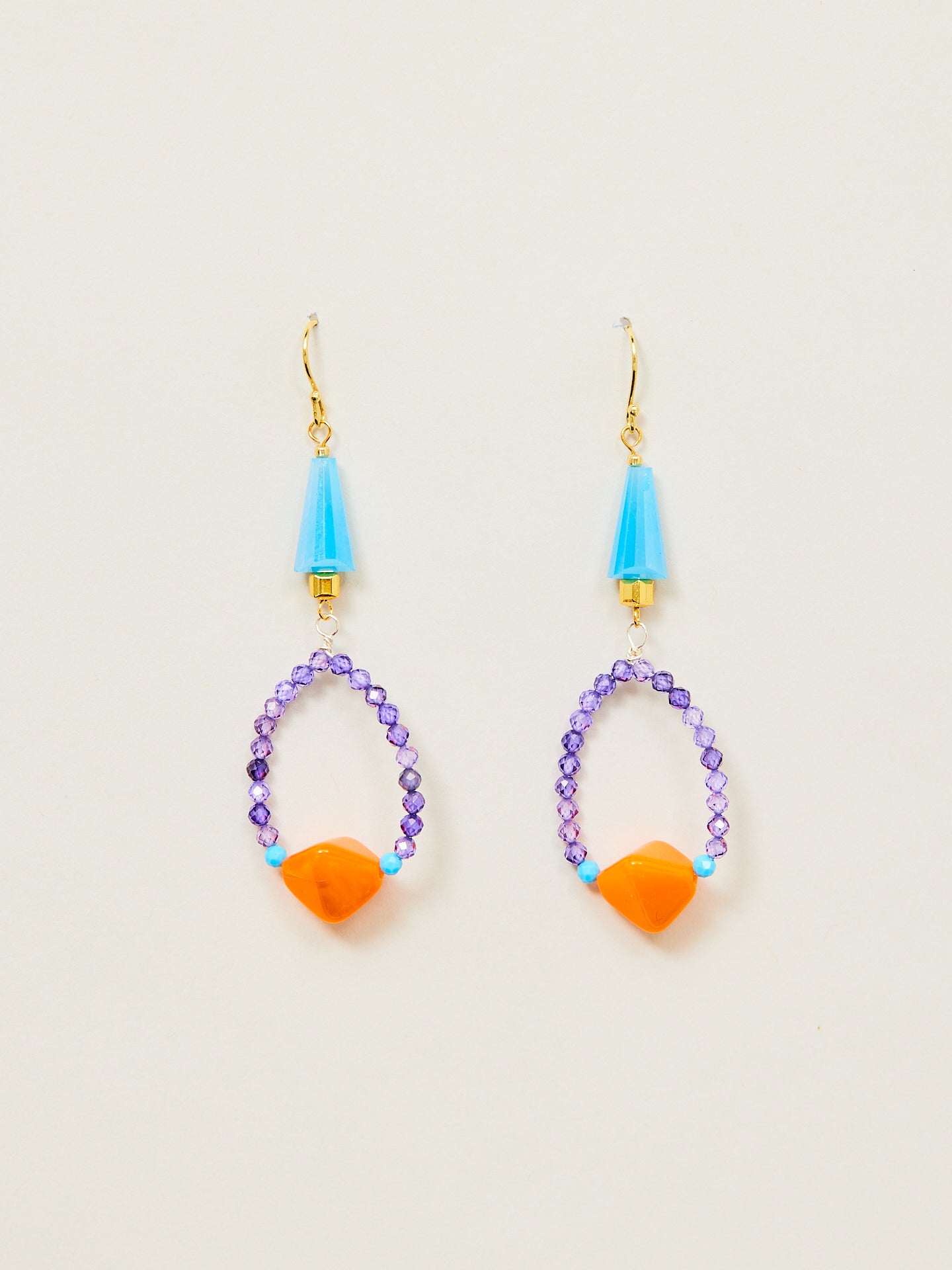 Großaufnahme zwier wunderschöner Ohrringe, bestehnd aus goldenen Ohrhängern, blauen, violetten und orangenen Perlen.