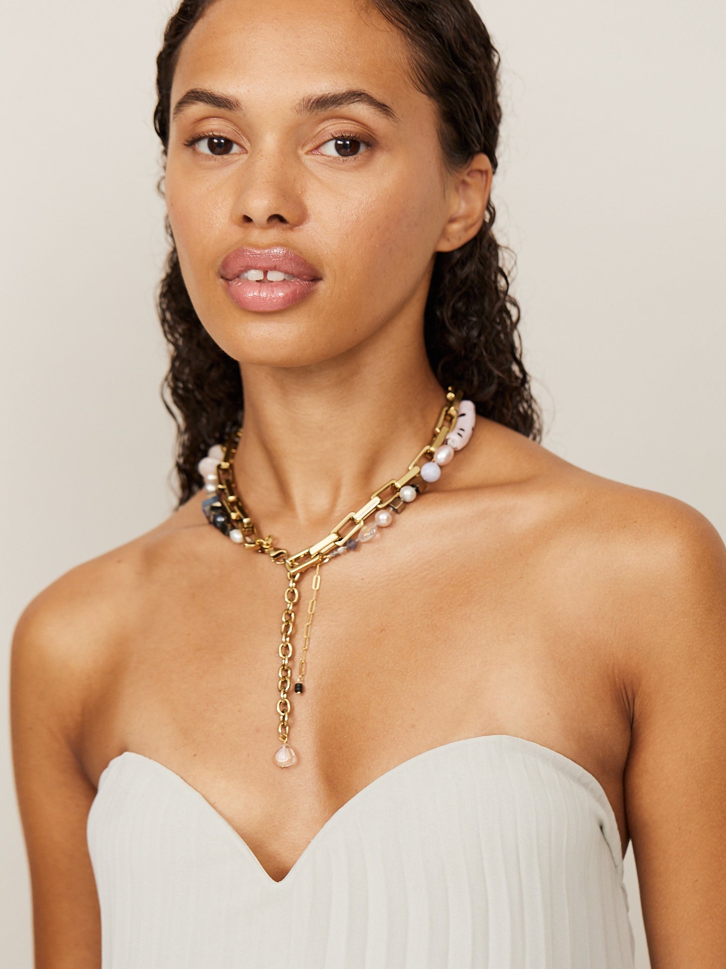 Frau trägt eine Kombination aus zwei goldenen Ketten mit hellen Perlen, die einen extravaganten Look unterstreichen.