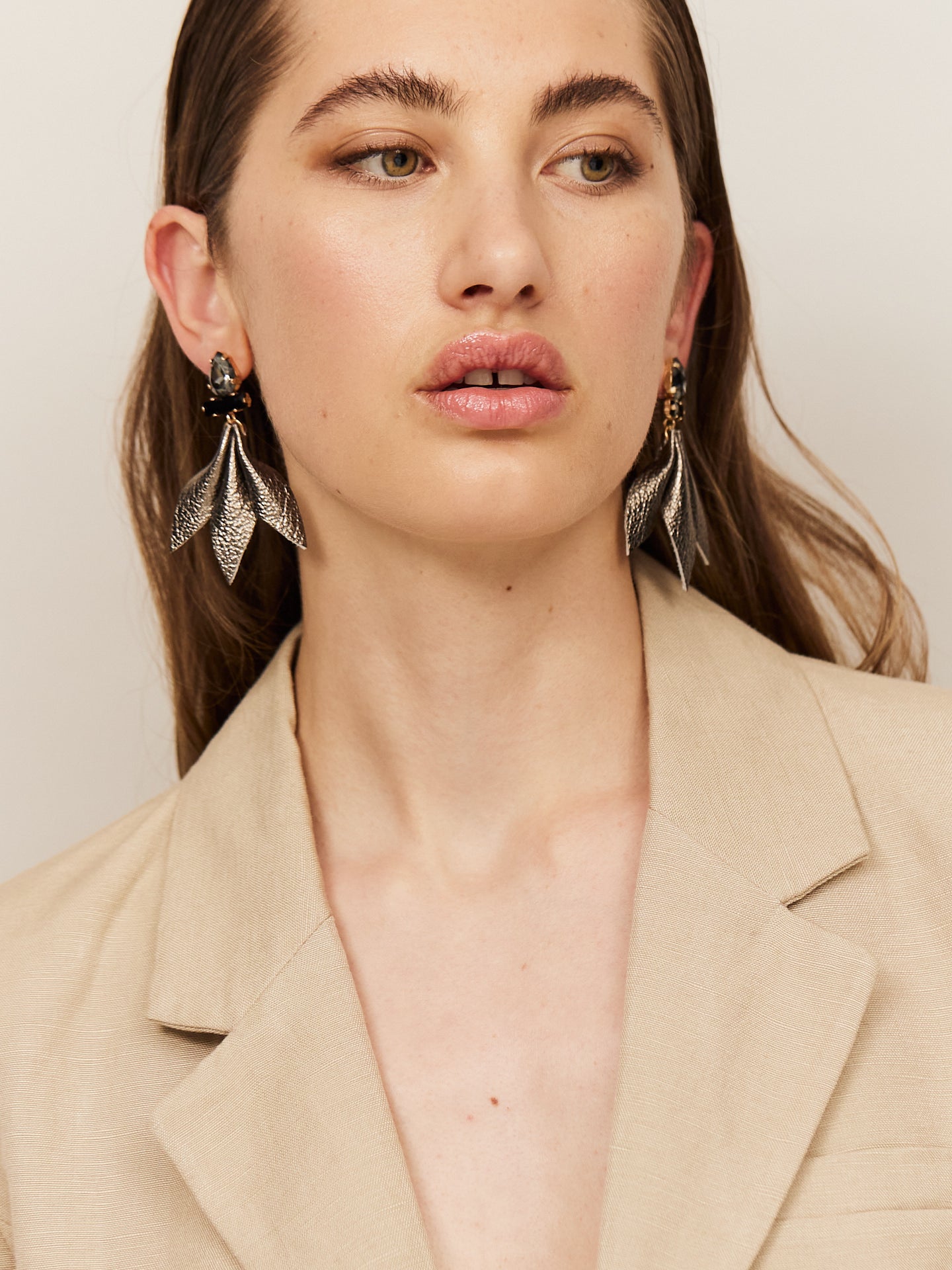 Attraktive Frau mit braunen Augen und sinnlichen Lippen, trägt einen hellen Blazer und helle Nappa Leder Ohrringe mit dunklem Stecker.