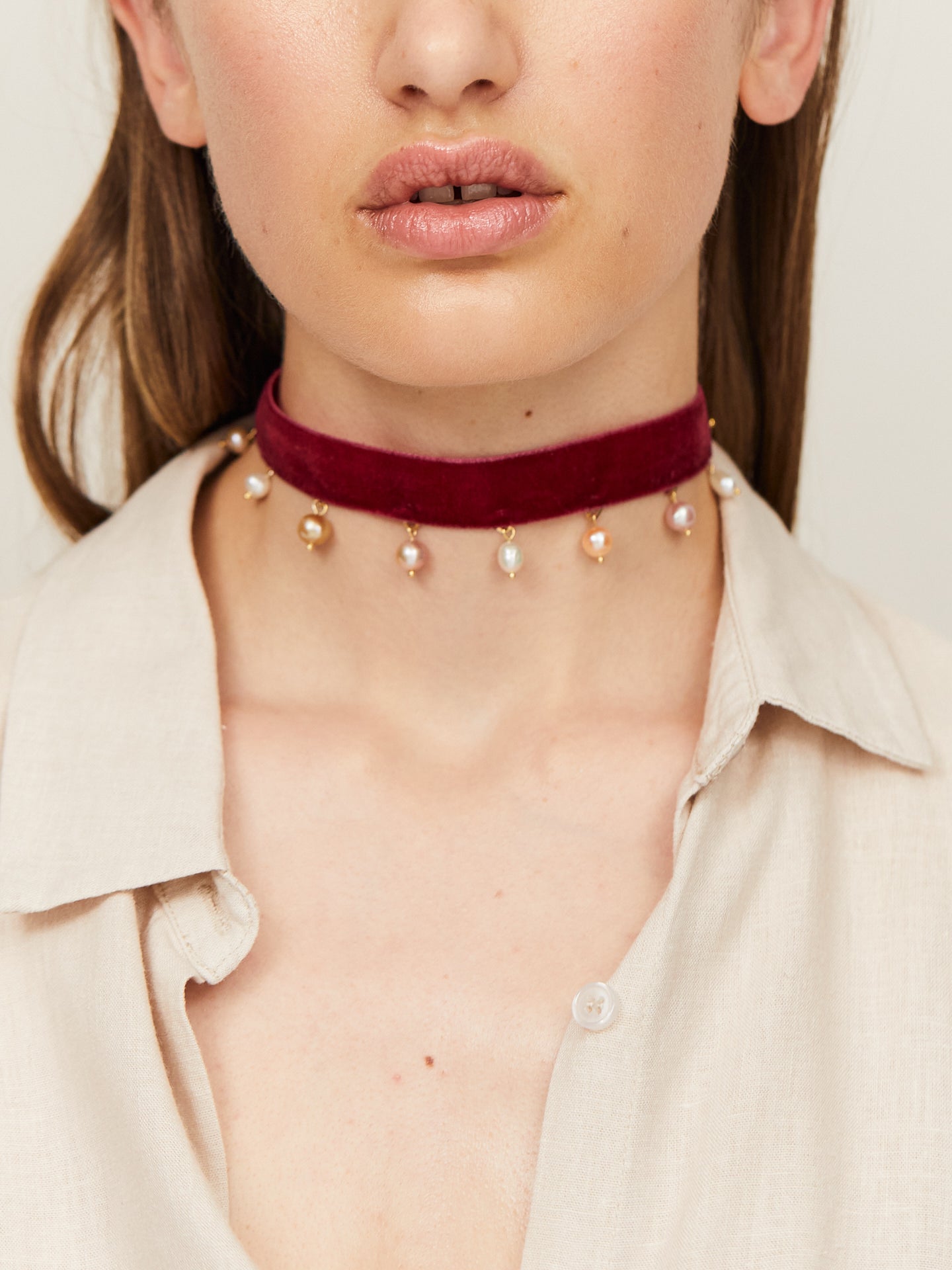 Eine Frau mit sinnlichen Lippen trägt einen handgefertigten Choker, an dem Perlen in Abständen hängen.